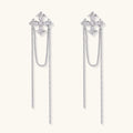 White gold plated baroque cross stud earrings with long cascading zirconia chains on cream background