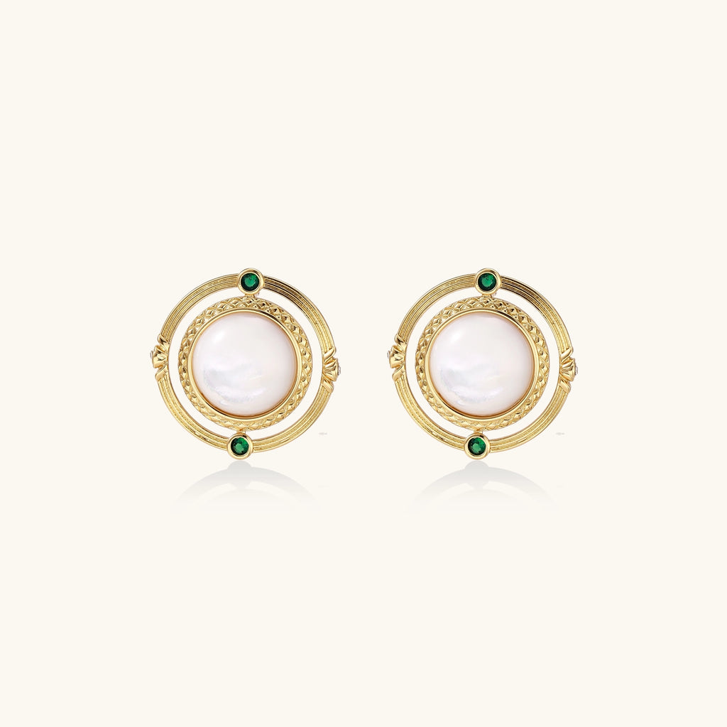 Circular gold stud earrings with iridescent mother-of-pearl center and green zirconia accents on cream background.