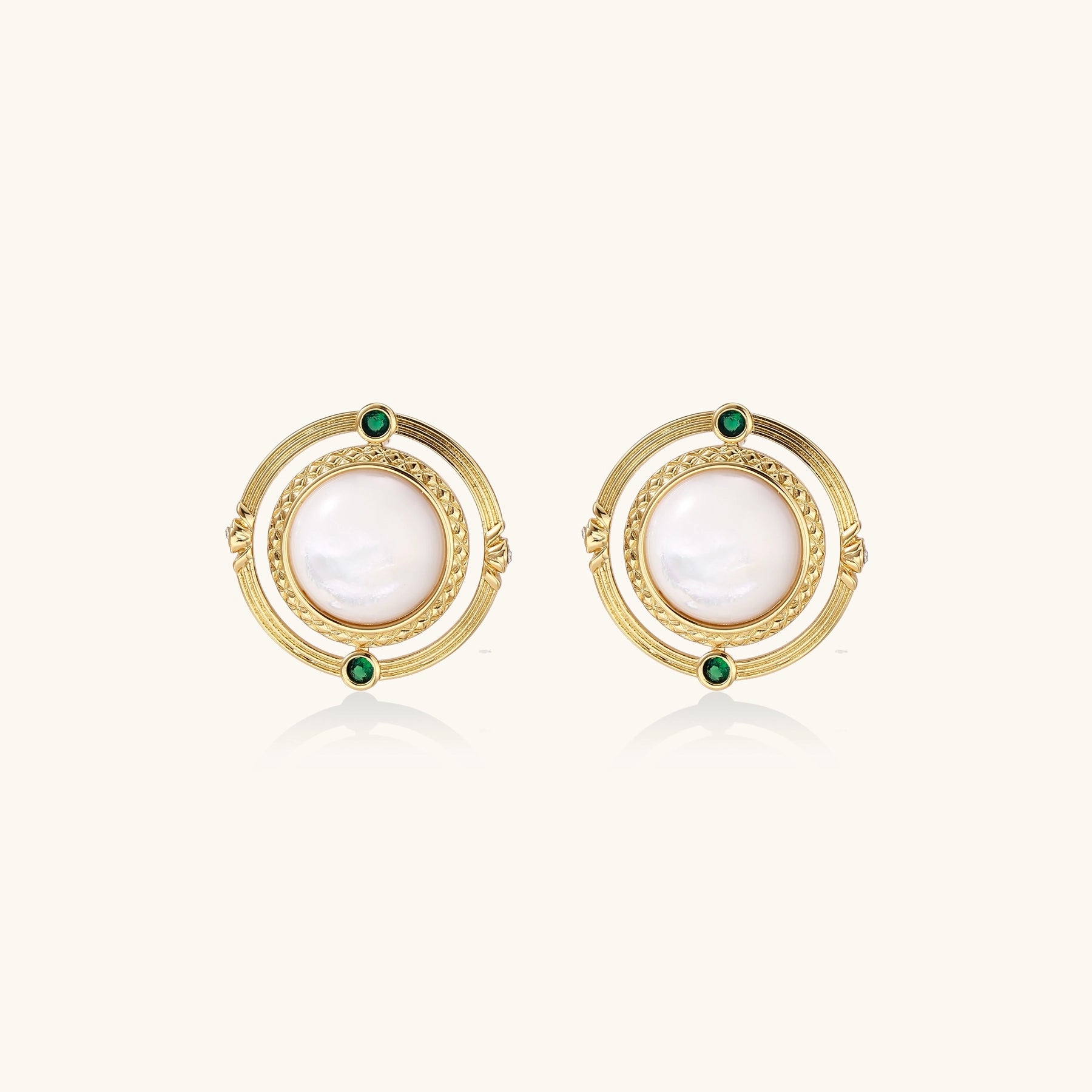 Circular gold stud earrings with iridescent mother-of-pearl center and green zirconia accents on cream background.