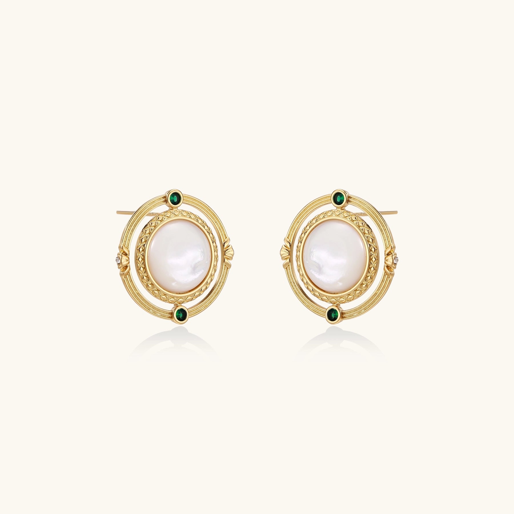 Circular gold stud earrings with iridescent mother-of-pearl center and green zirconia accents on cream background.