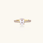 Gold-plated solitaire ring with oval zirconia center stone and pavé band on cream background