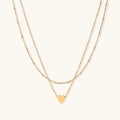 Delicate double-chain gold necklace with tiny heart pendant on cream background