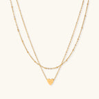 Delicate double-chain gold necklace with tiny heart pendant on cream background