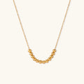 Delicate gold-plated necklace with graduated spherical beads forming gentle smile curve on beige background