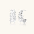 White gold plated sculptural hoop earrings with organic wavy edges and reflective metallic finish on cream background