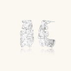 White gold plated sculptural hoop earrings with organic wavy edges and reflective metallic finish on cream background