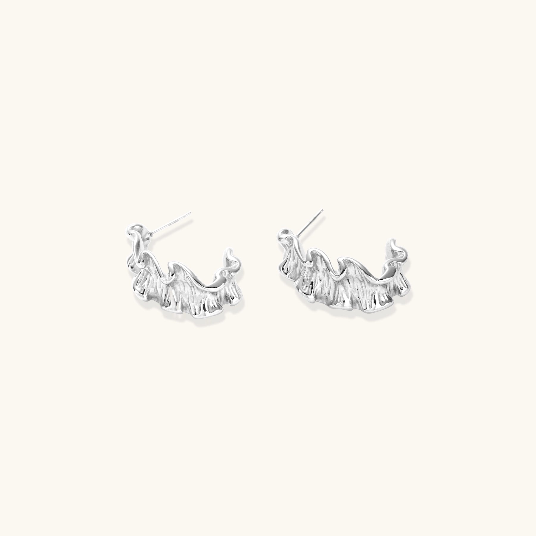 White gold plated sculptural hoop earrings with organic wavy edges and reflective metallic finish on cream background