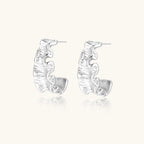White gold plated sculptural hoop earrings with organic wavy edges and reflective metallic finish on cream background