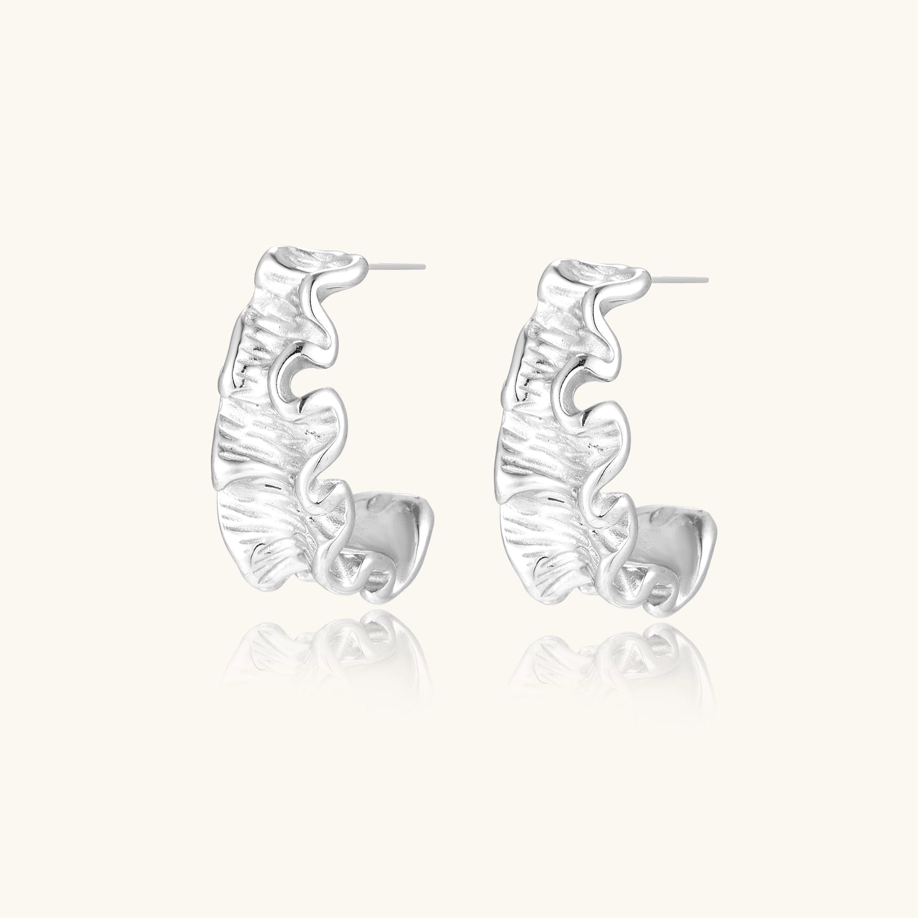 White gold plated sculptural hoop earrings with organic wavy edges and reflective metallic finish on cream background