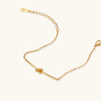 Delicate gold chain bracelet with minimalist bar and centered knot detail on cream background