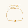 Delicate gold chain bracelet with minimalist bar and centered knot detail on cream background