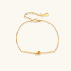 Delicate gold chain bracelet with minimalist bar and centered knot detail on cream background