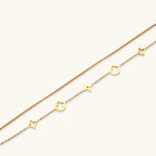Double-layer gold-plated bracelet with quatrefoil and star charms on cream background, 18K gold finish.