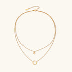 Gold layered necklace set with sunburst and smiley face pendants on delicate chains against white background.