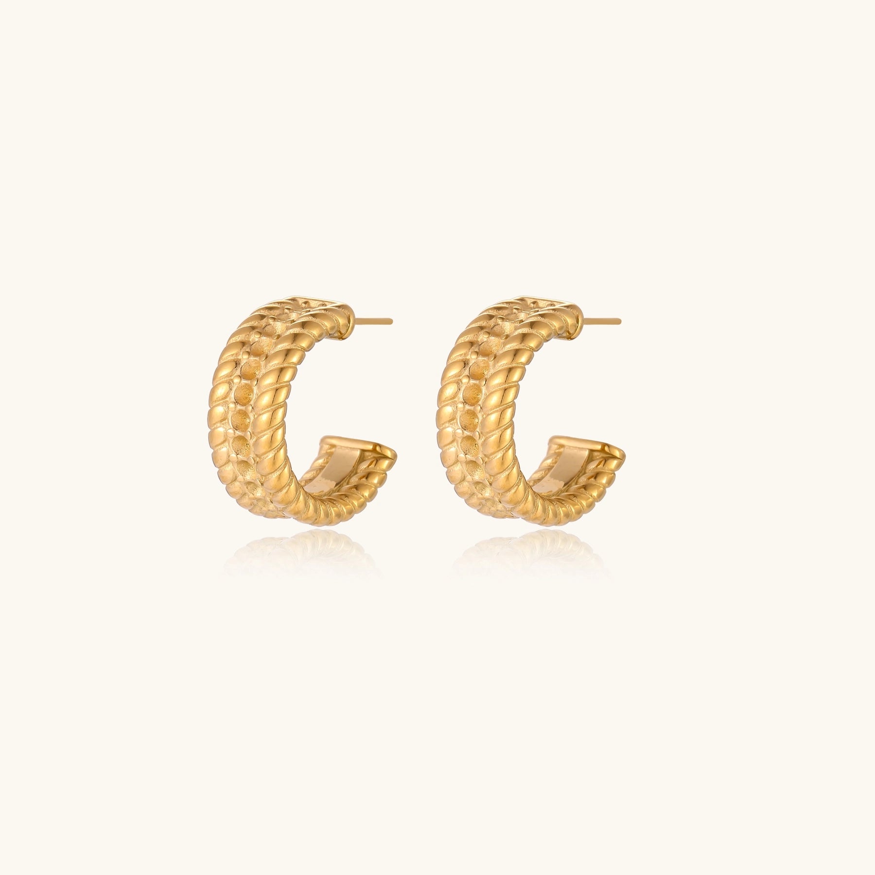 Textured gold huggie hoop earrings with raised ribbed rows creating dimensional sculptural design on cream background