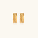 Textured gold huggie hoop earrings with raised ribbed rows creating dimensional sculptural design on cream background
