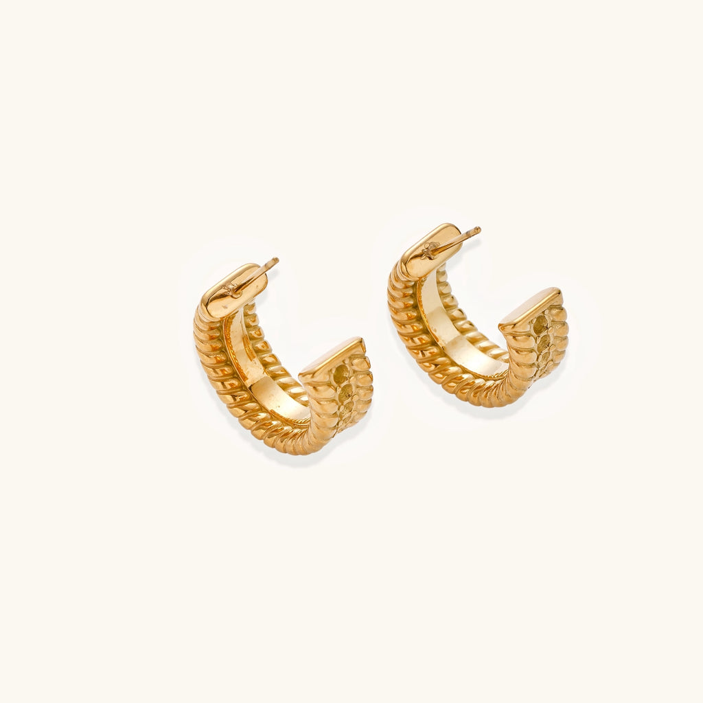 Textured gold huggie hoop earrings with raised ribbed rows creating dimensional sculptural design on cream background