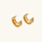 Textured gold huggie hoop earrings with raised ribbed rows creating dimensional sculptural design on cream background