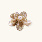 Flower-shaped brooch with iridescent shell petals, freshwater pearl center, and gold-plated radiating details.