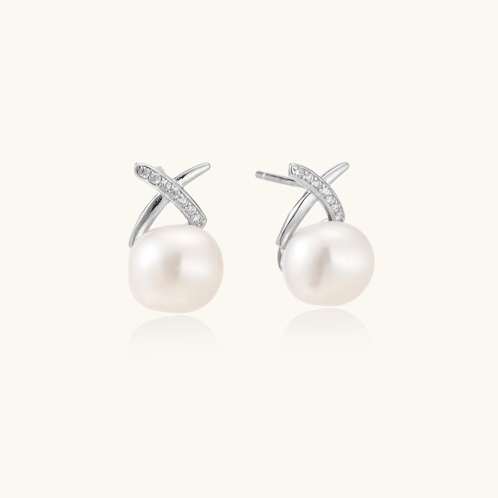 Rhodium-plated silver stud earrings with sparkling X design above lustrous round freshwater pearls on white background.