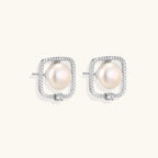 Rhodium-plated silver stud earrings with cushion frame, centered freshwater pearl, and tiny crystal accent