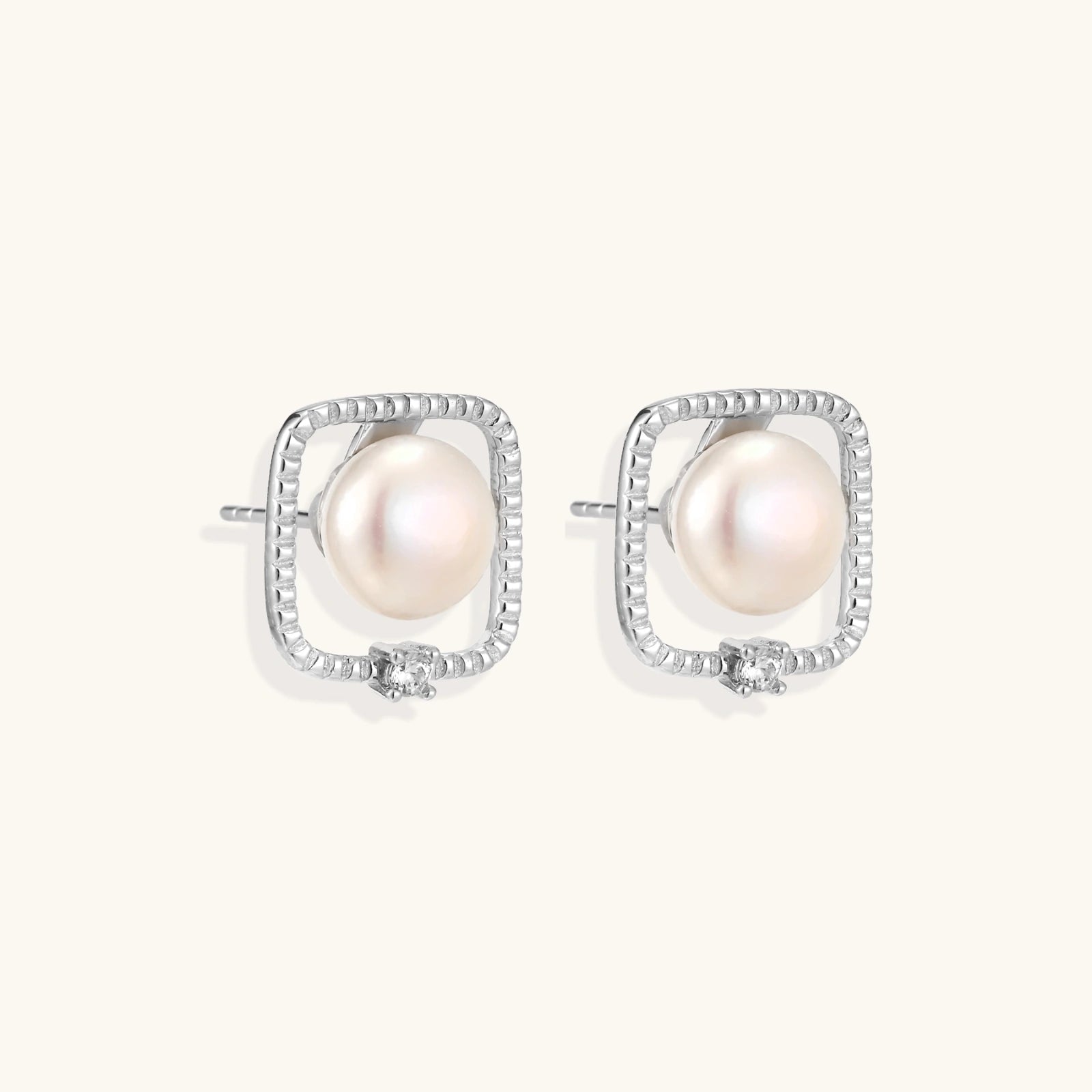 Rhodium-plated silver stud earrings with cushion frame, centered freshwater pearl, and tiny crystal accent